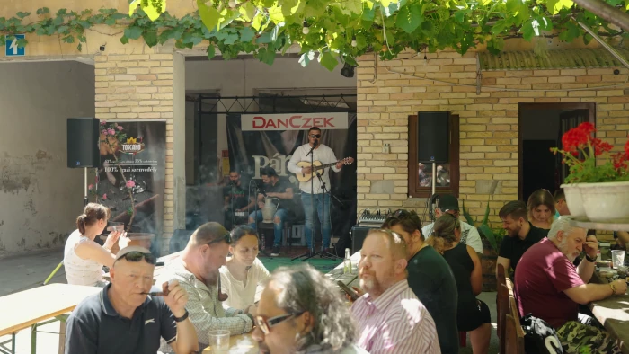 Hangulatos kerthelyiség asztalokkal, háttérben zenészekkel